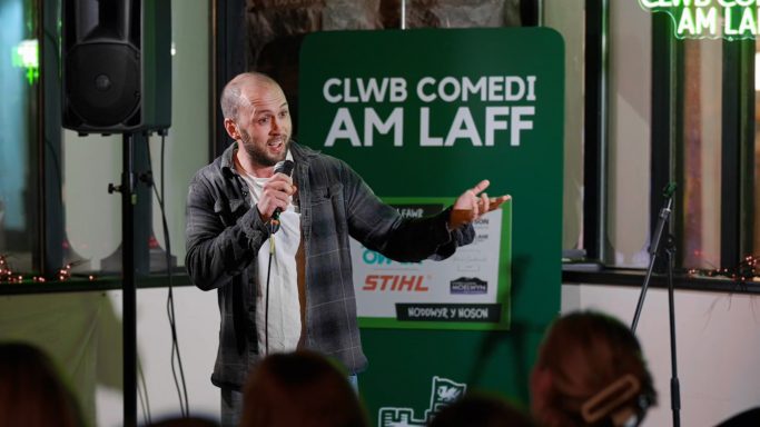 A comedian performing on stage with a microphone at a comedy club.