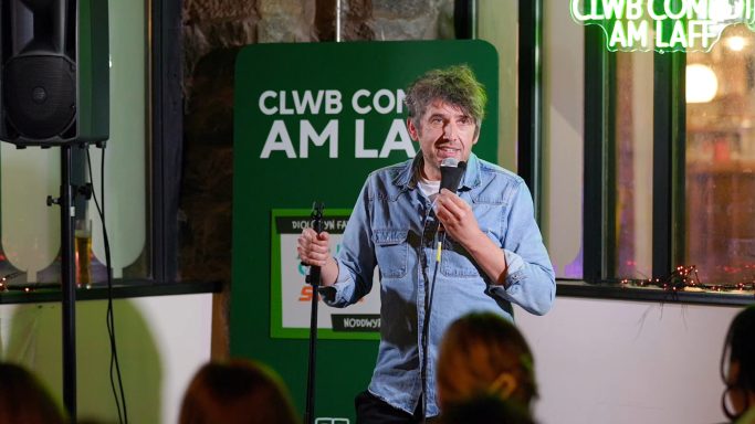 A comedian performs on stage with a microphone in a lively venue.